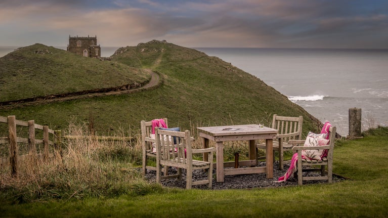 A table and four chairs in the grassed garden shared by Carnweather and the other holiday apartments at Doyden House, overlooking a folly castle and the sea, Cornwall
